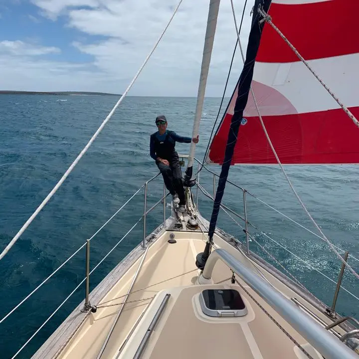 Deirdre Sibly on the bow of a sailboat with a red and white sail.