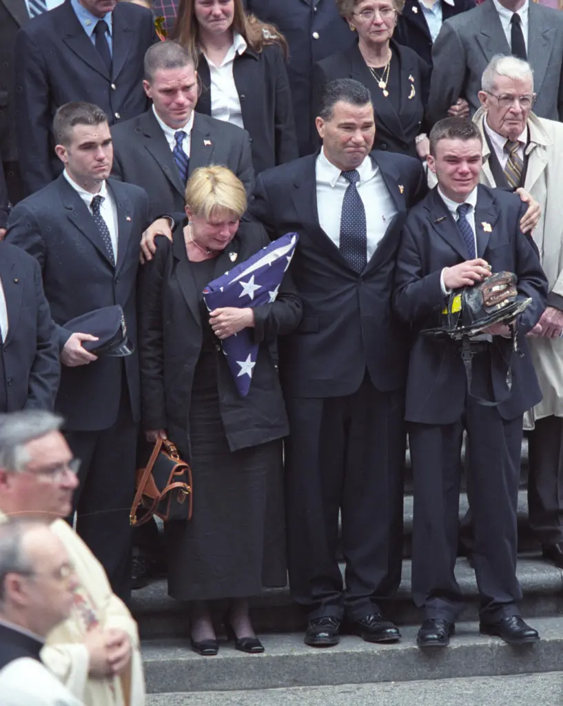 Family members of Firefighter James Riches leave Saint Patrick's Cathedral after his funeral, including his mother Rita holding a folded American flag, his father James, a Battalion Chief, and his three brothers.