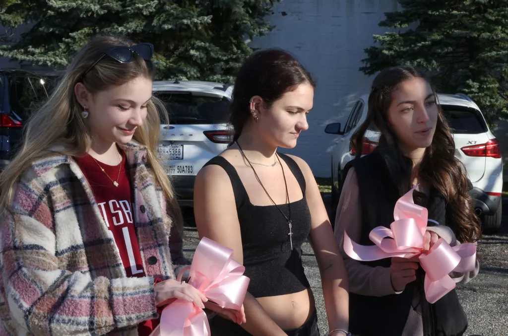 Three young women holding pink ribbons, remembering Emily Finn.