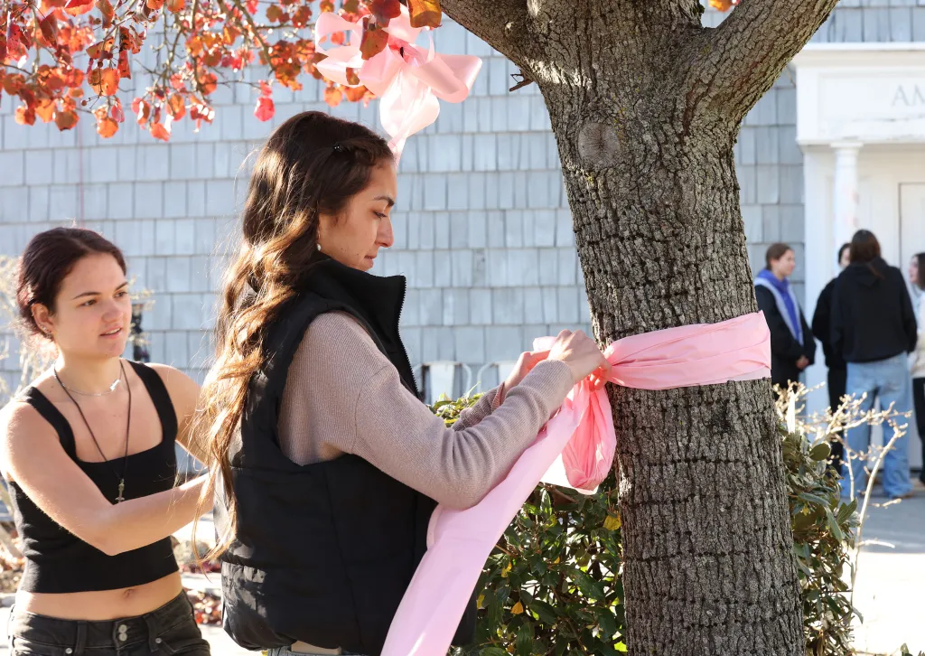 Two young women tying pink ribbons around a tree in memory of Emily Finn.