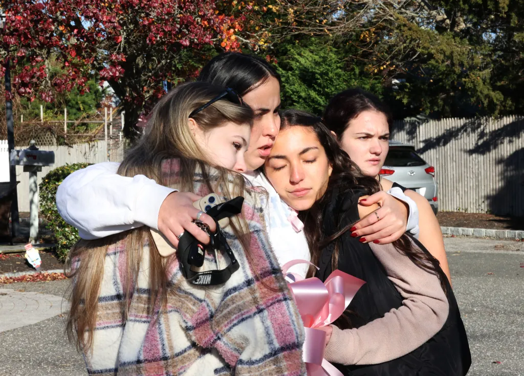 Four young women embrace while holding pink ribbons in memory of Emily Finn.
