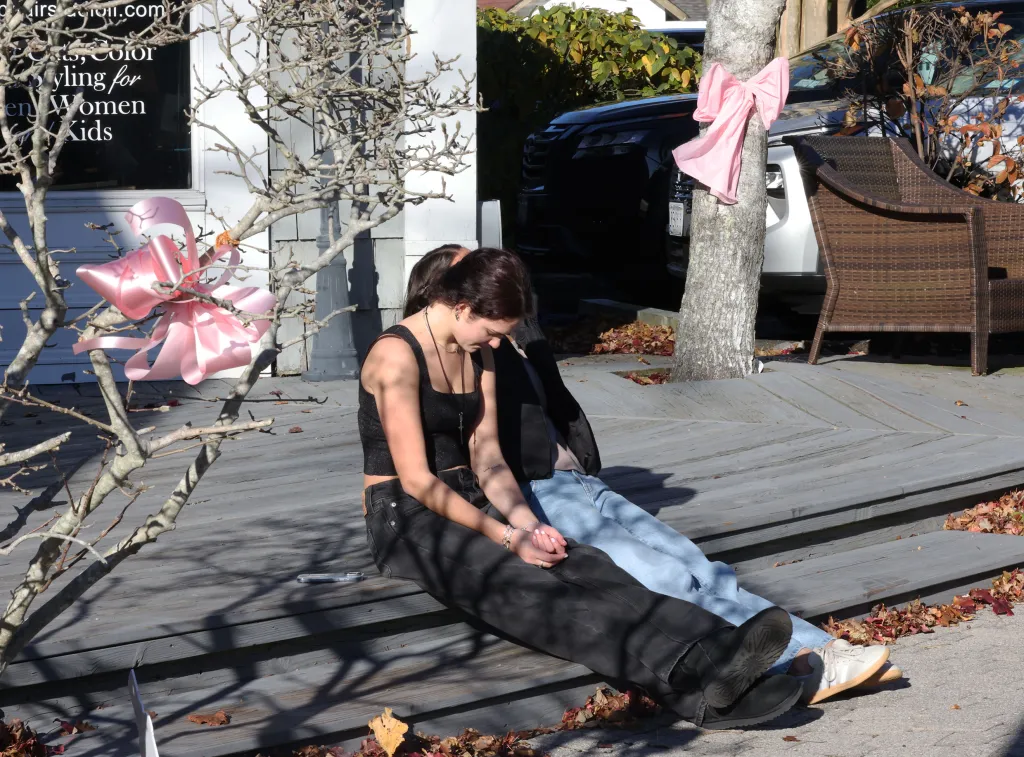 Brynne Ballan and Maya Truglio sitting on a wooden porch with pink ribbons tied to trees.