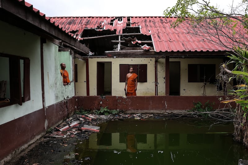 Monks stand near a damaged dorm at Thai Niyom temple, which was hit by Cambodian artillery