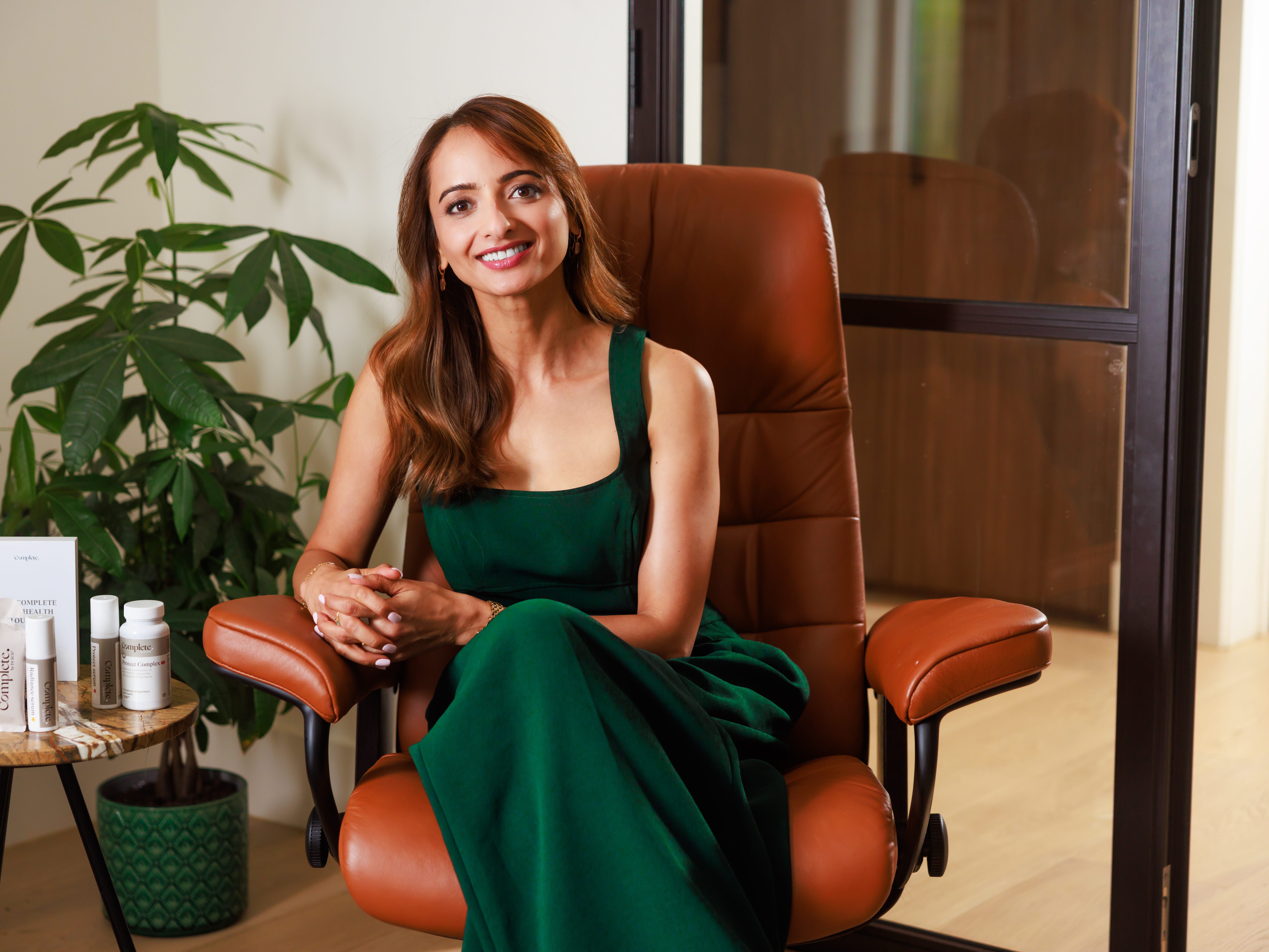 A woman wears a green dress and sits on a leather chair.