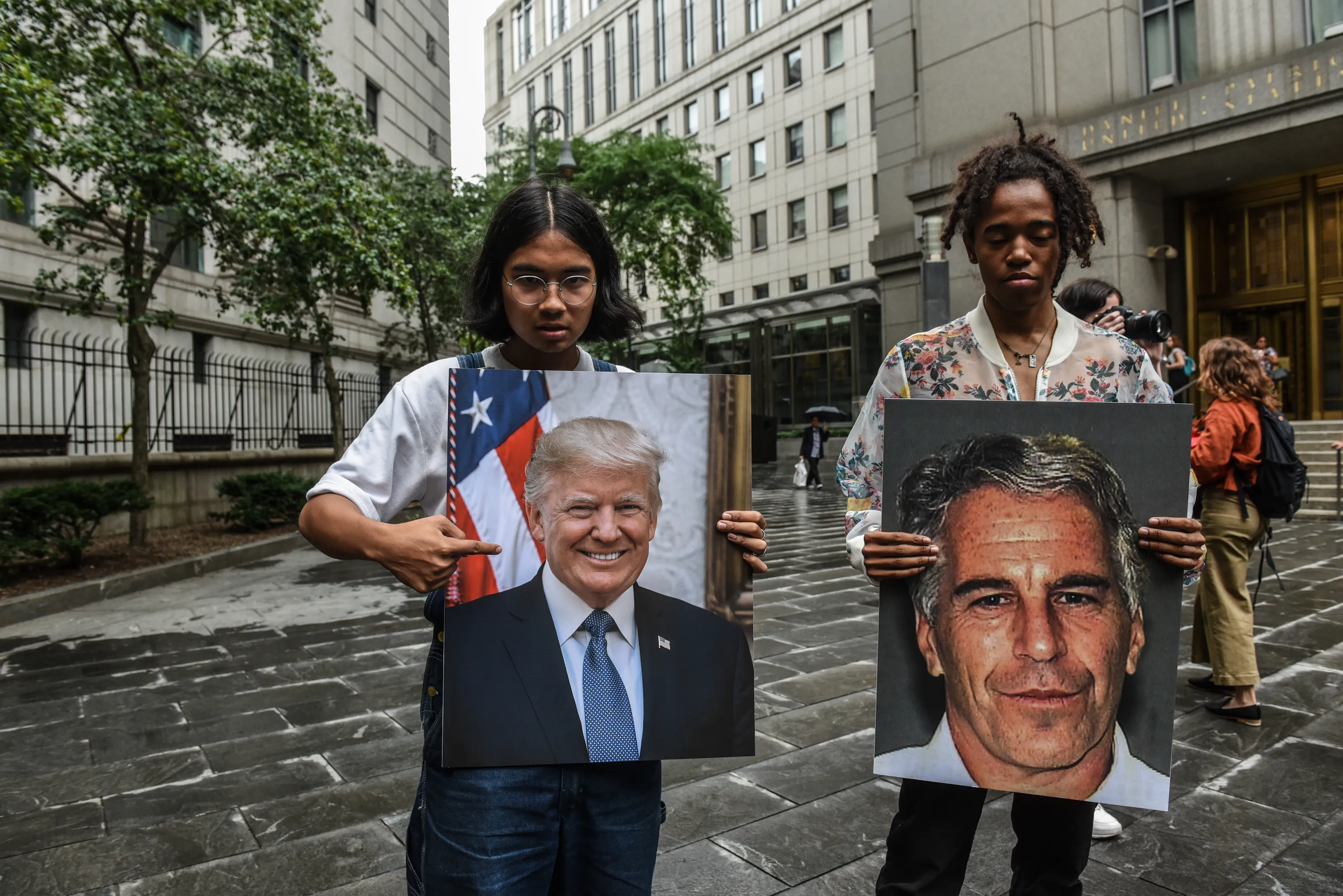 Protesters hold up large photos of Jeffrey Epstein and President Donald Trump on the steps of a courthouse.