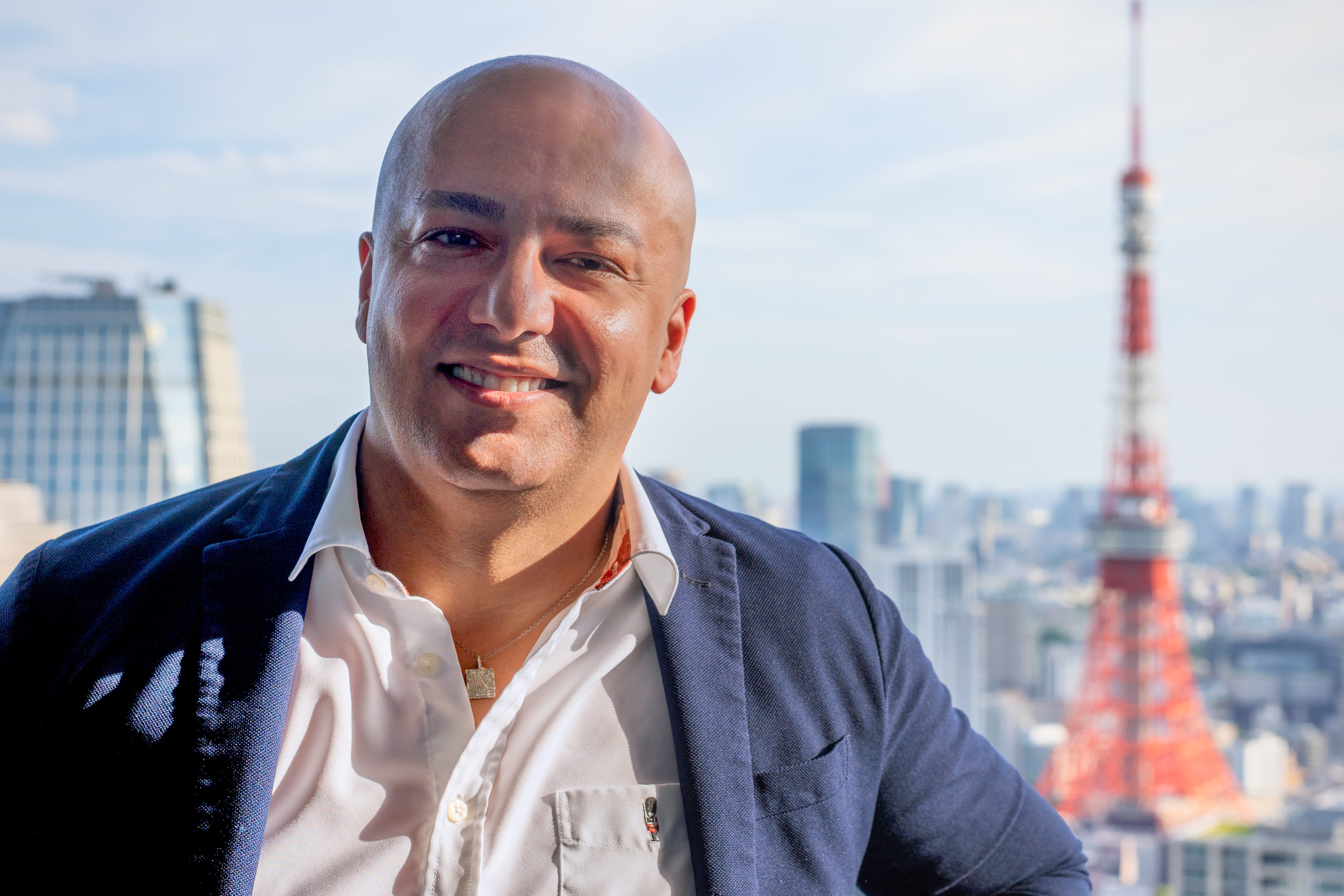 Jad Tarifi, wearing a white shirt and suit, is posing in front of the Tokyo Tower.