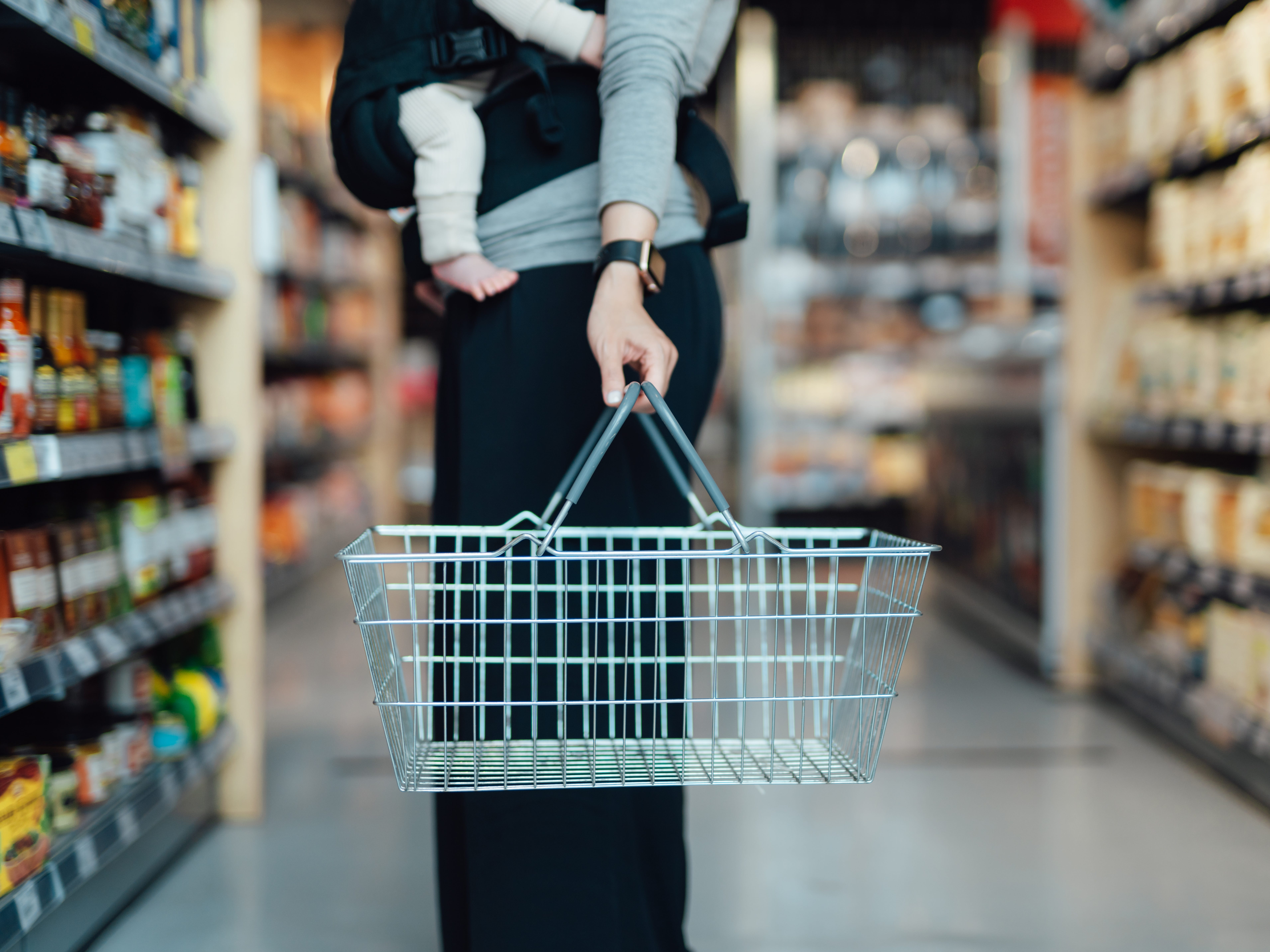 A woman with a baby and an empty shopping basket in a grocery store.