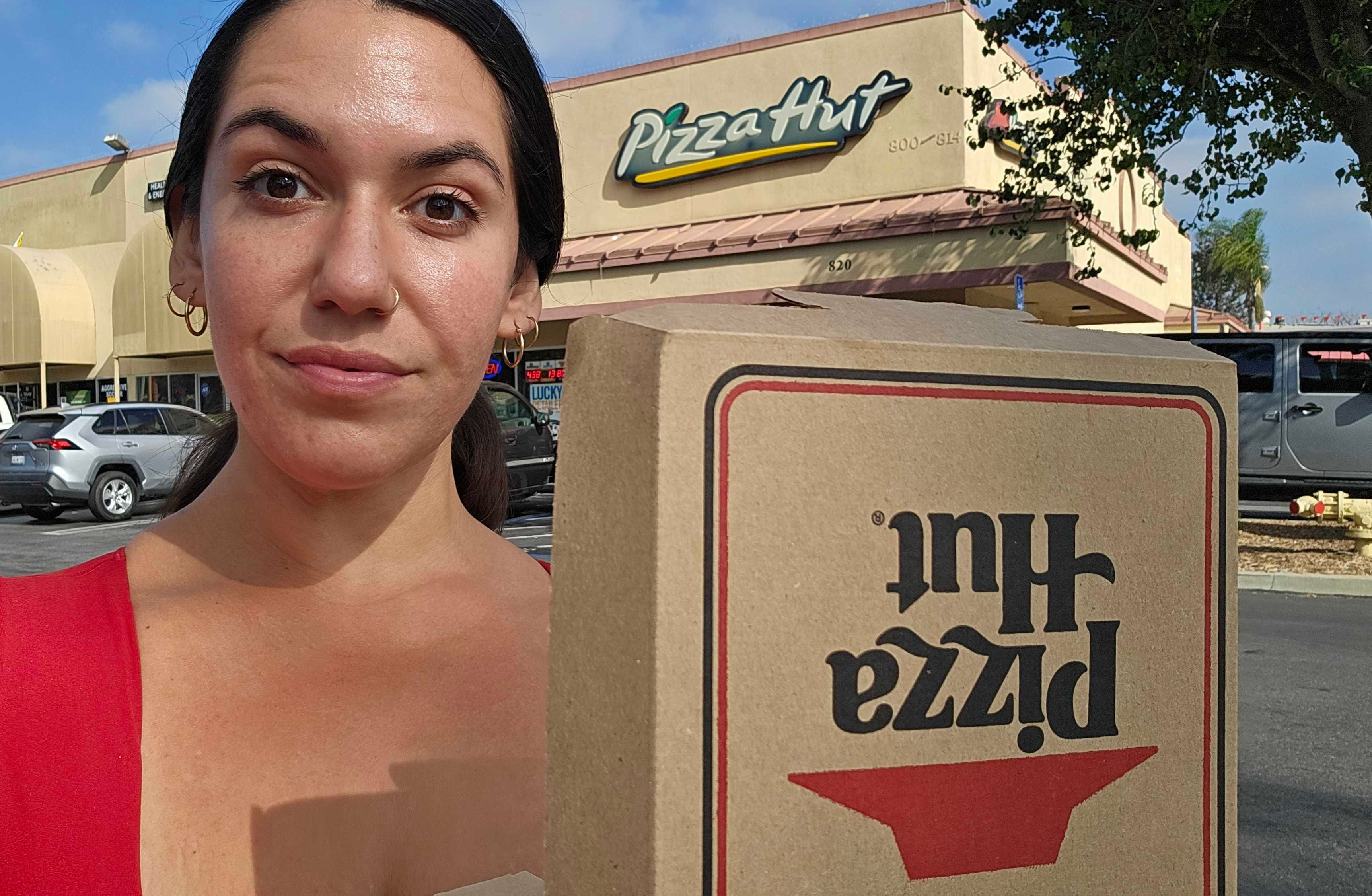 The author poses with a Pizza Hut box in front of one of he restaurants.