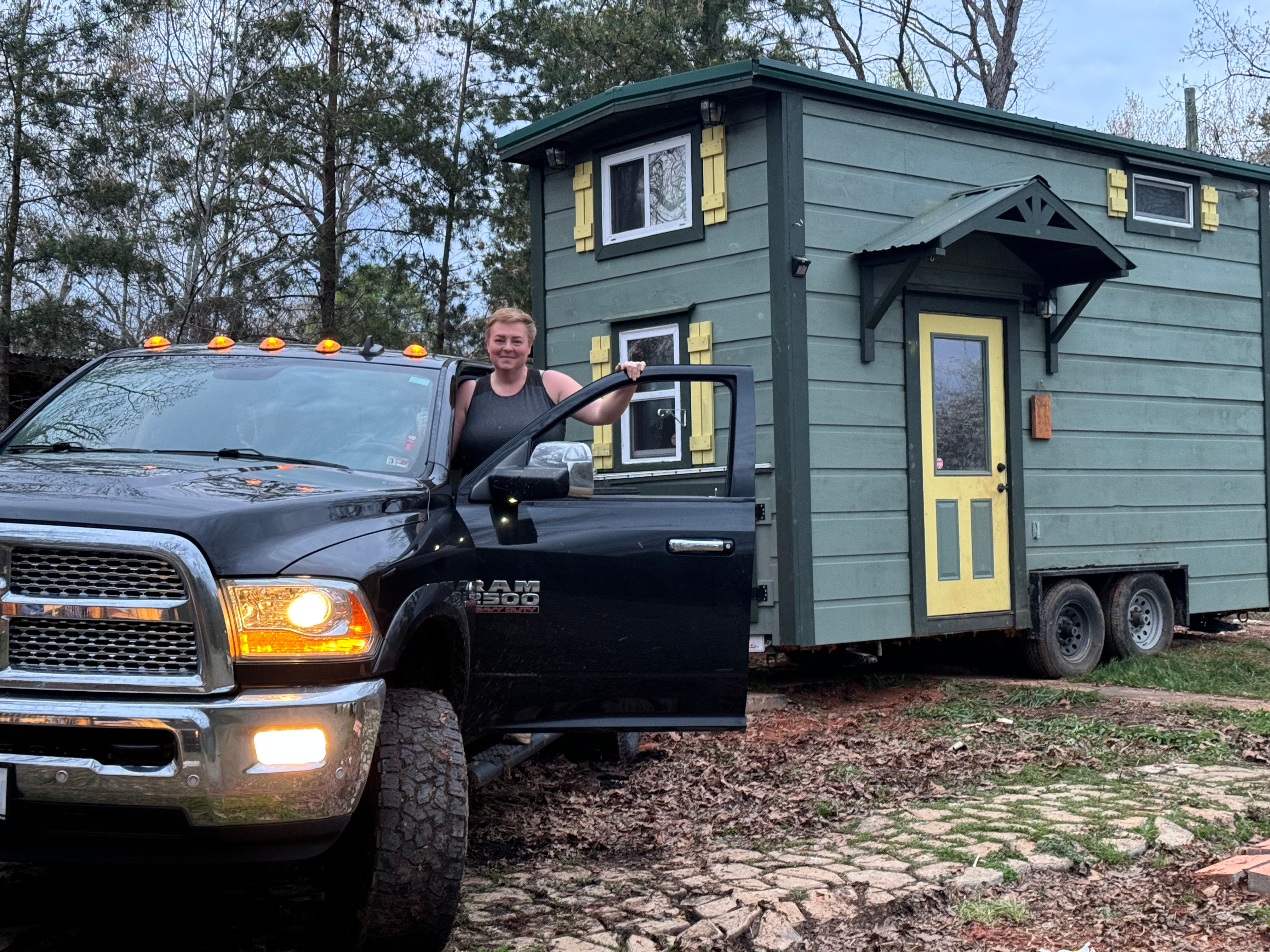 A woman standing on a truck hauling a tiny home.