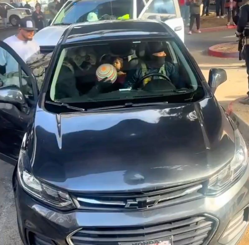 With one masked officer in the driver's seat, another in the passenger seat throws a beachball into the face of the child sitting in the back seat.