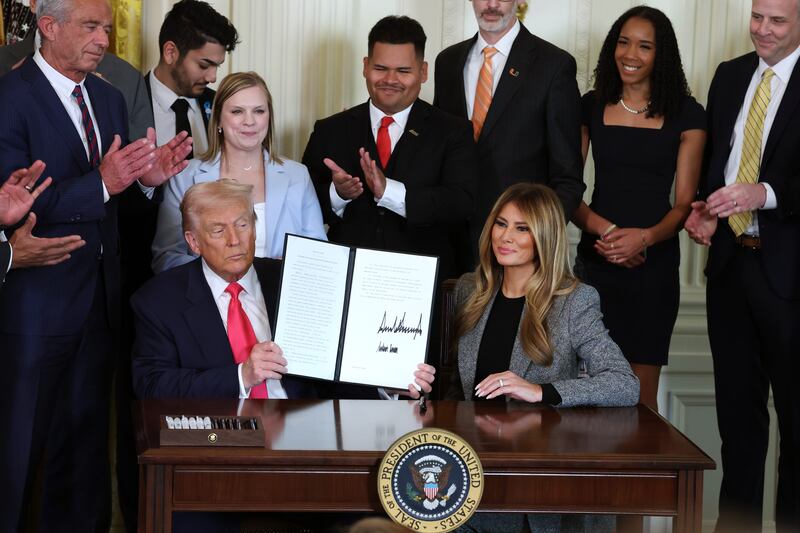 WASHINGTON, DC - NOVEMBER 13: U.S. President Donald Trump, joined by first lady Melania Trump, members of his administration and foster care advocates, holds up a copy of the "Fostering the Future" executive order after signing the order in the East Room of the White House on November 13, 2025 in Washington, DC. The executive order, championed by first lady Melania Trump, works to expand opportunities for education, career development, housing and other resources for youth transitioning from foster care to adulthood. (Photo by Anna Moneymaker/Getty Images)