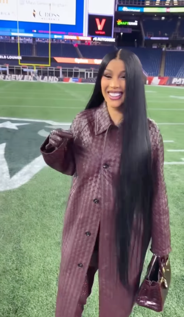 Cardi B in a head-to-toe maroon woven leather outfit at a football stadium.
