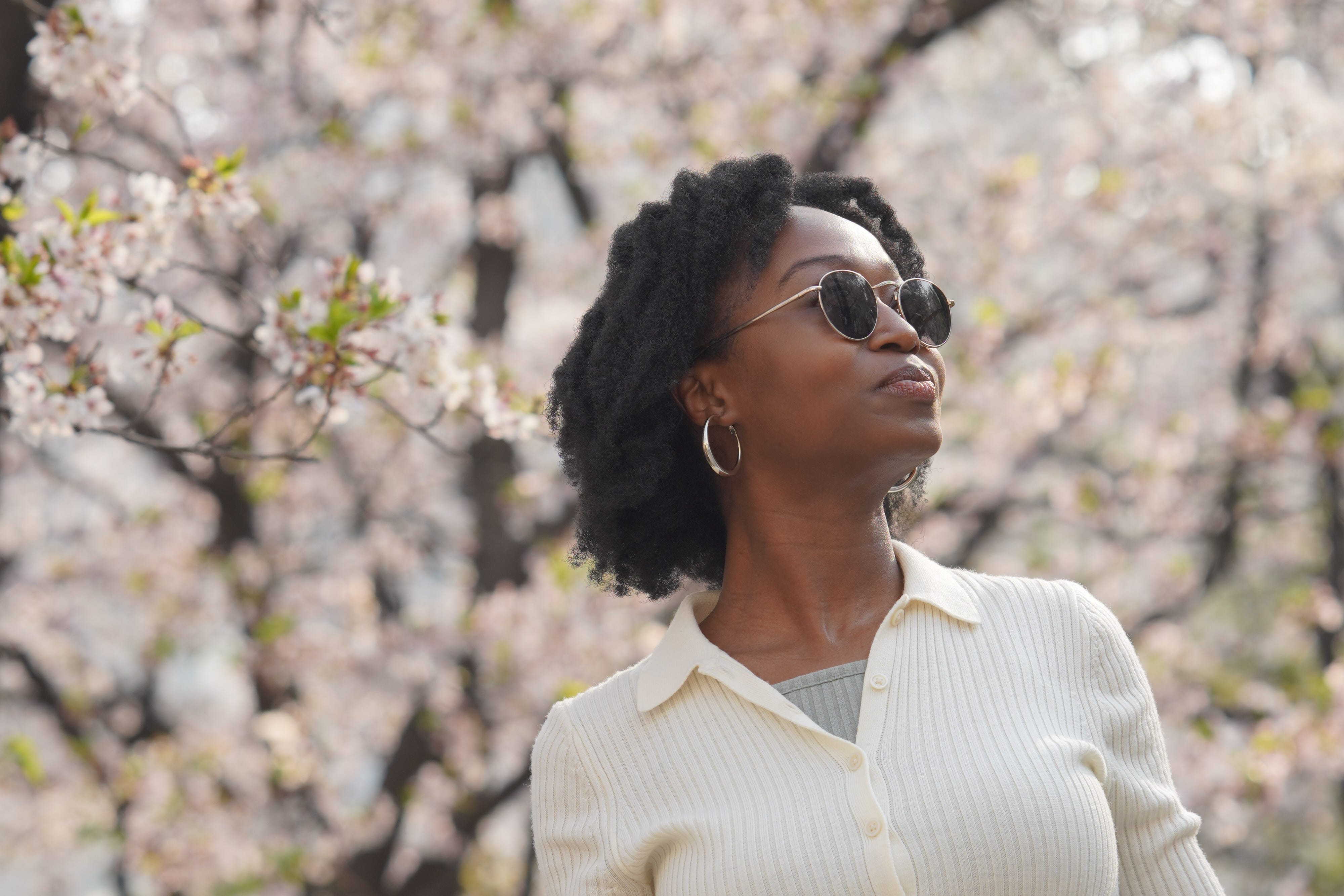 A woman posing in front of cherry blossom trees.