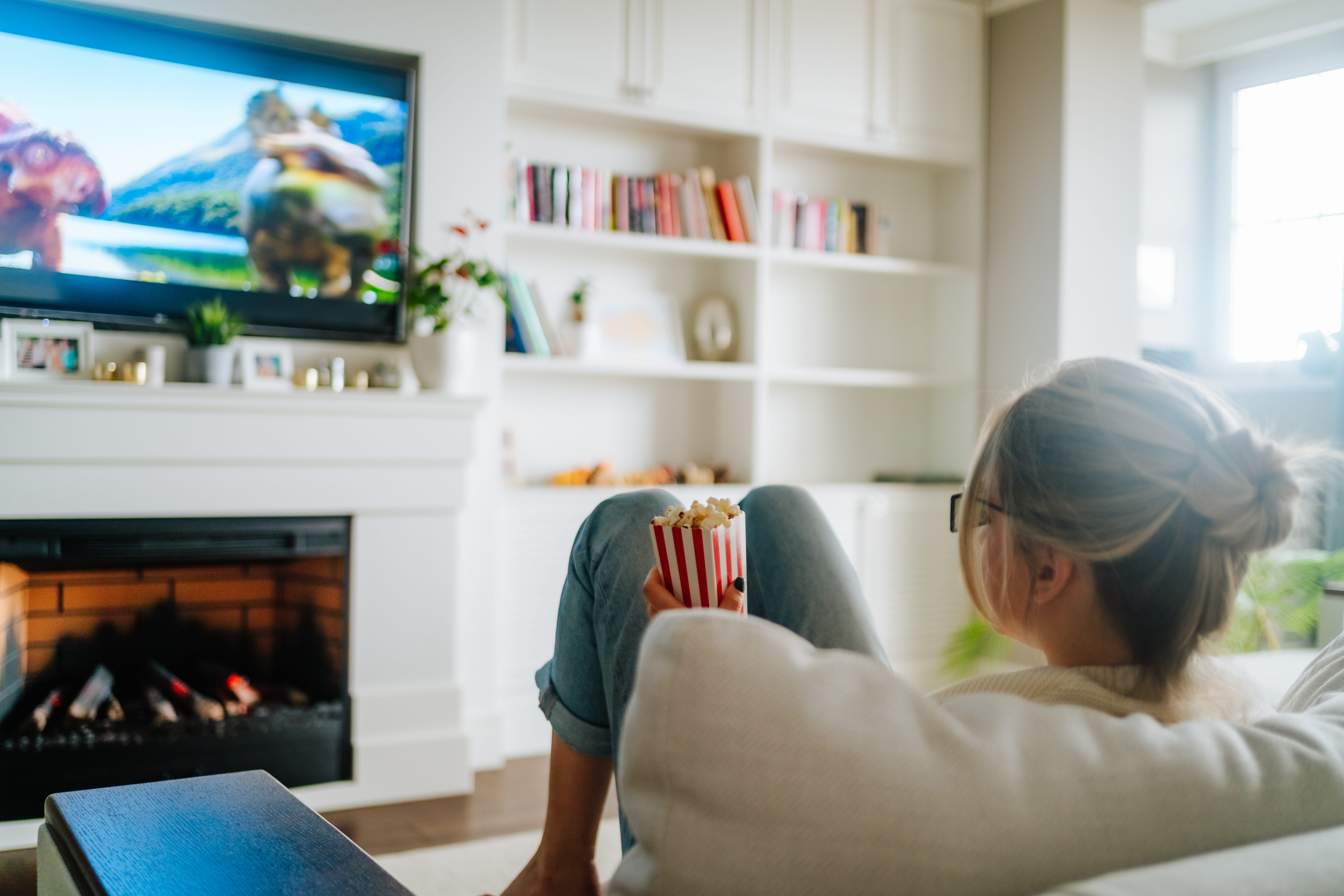 a woman watching tv while eating popcorn and sitting on the couch