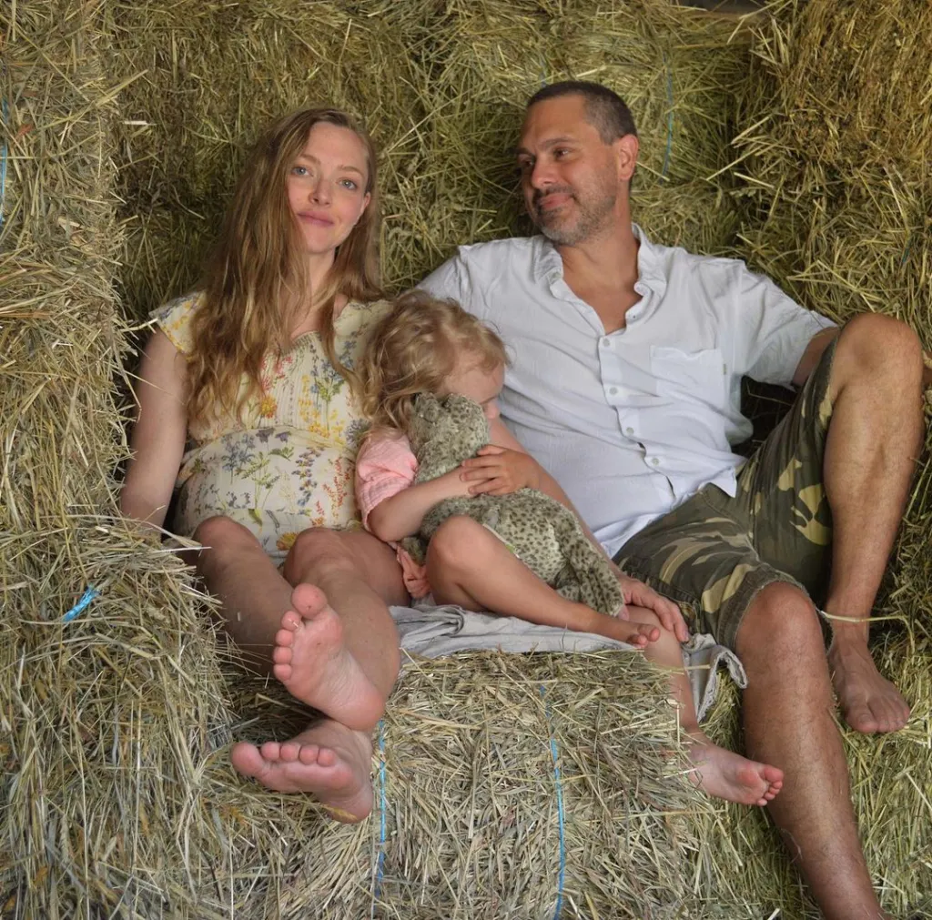 Amanda Seyfried, her husband, and young child sitting on hay bales.