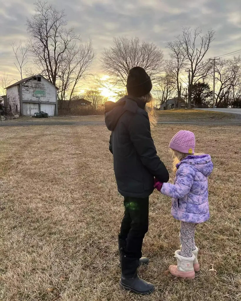 Amanda Seyfried with her children, holding hands and standing in a field at sunset.