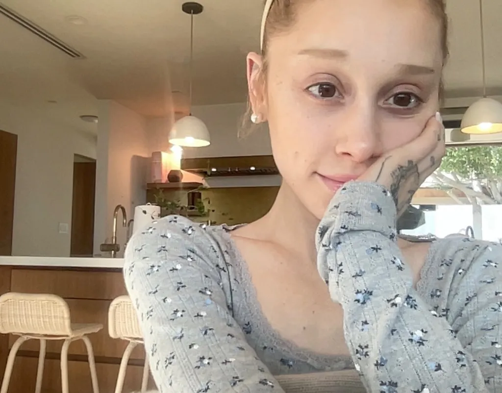 Ariana Grande with her hand on her cheek, wearing a grey floral top.