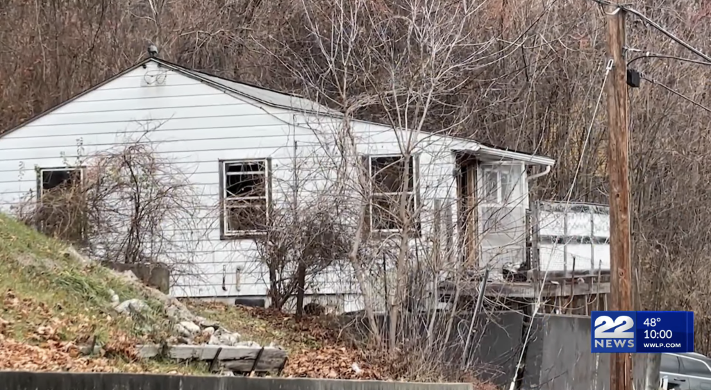 A white house with a partially collapsed porch, surrounded by bare trees.