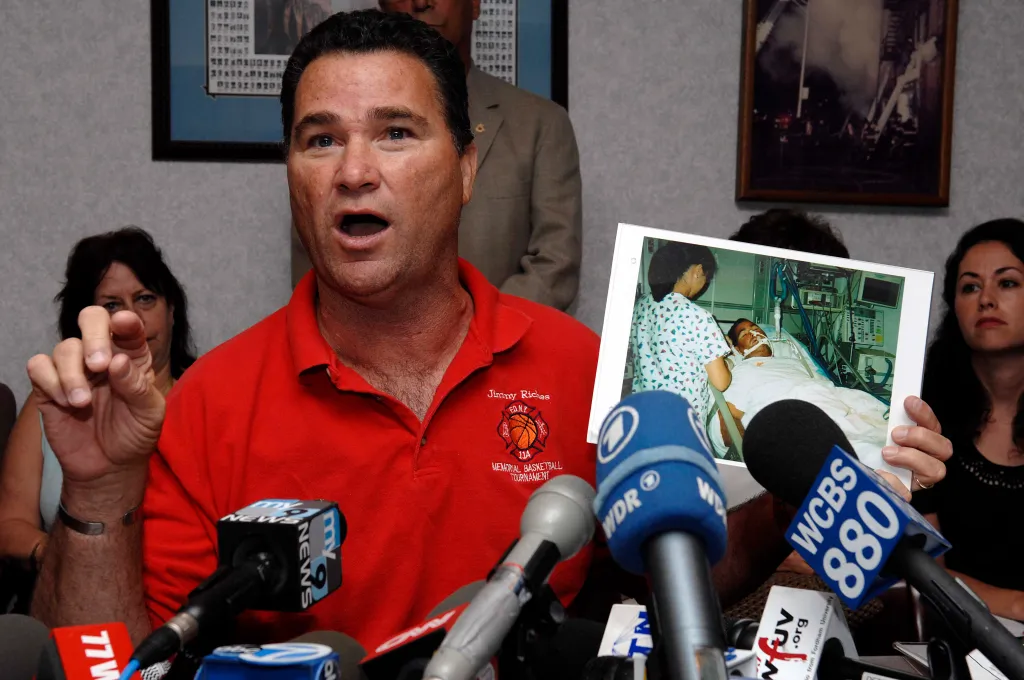 Deputy Chief Jim Riches speaking at a press conference, holding a photo of his son in a hospital bed.