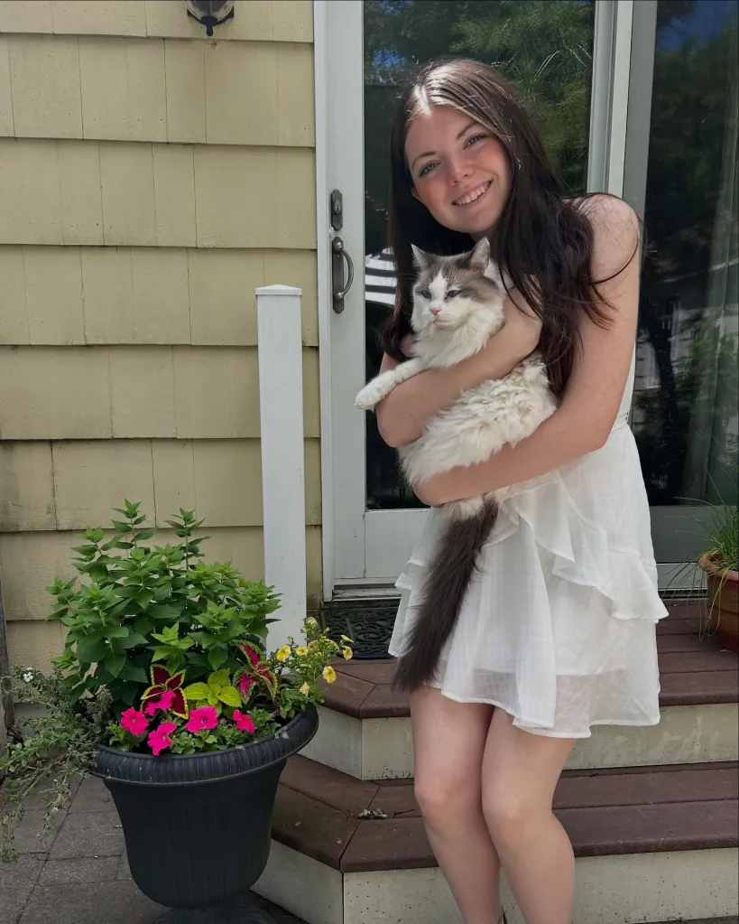 Emily Finn, 18, smiling and holding a cat on a porch.