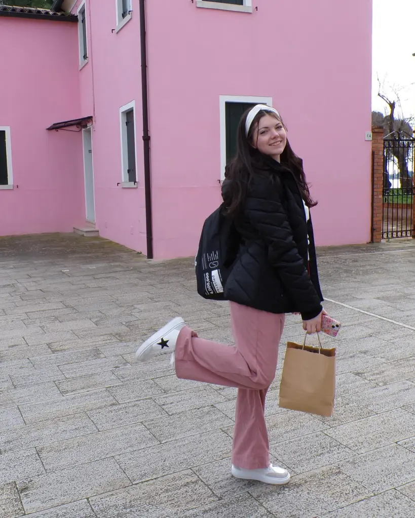 Emily Finn, an 18-year-old college student, stands smiling in front of a pink building, holding a paper bag and a cell phone.