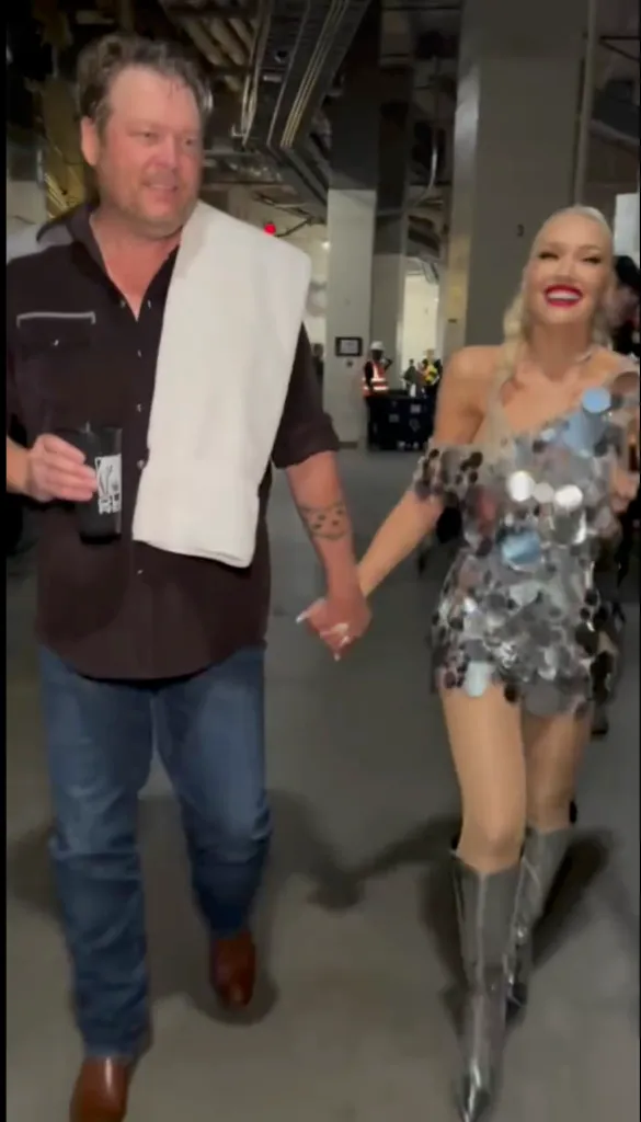 Blake Shelton and Gwen Stefani holding hands, walking in a hallway.