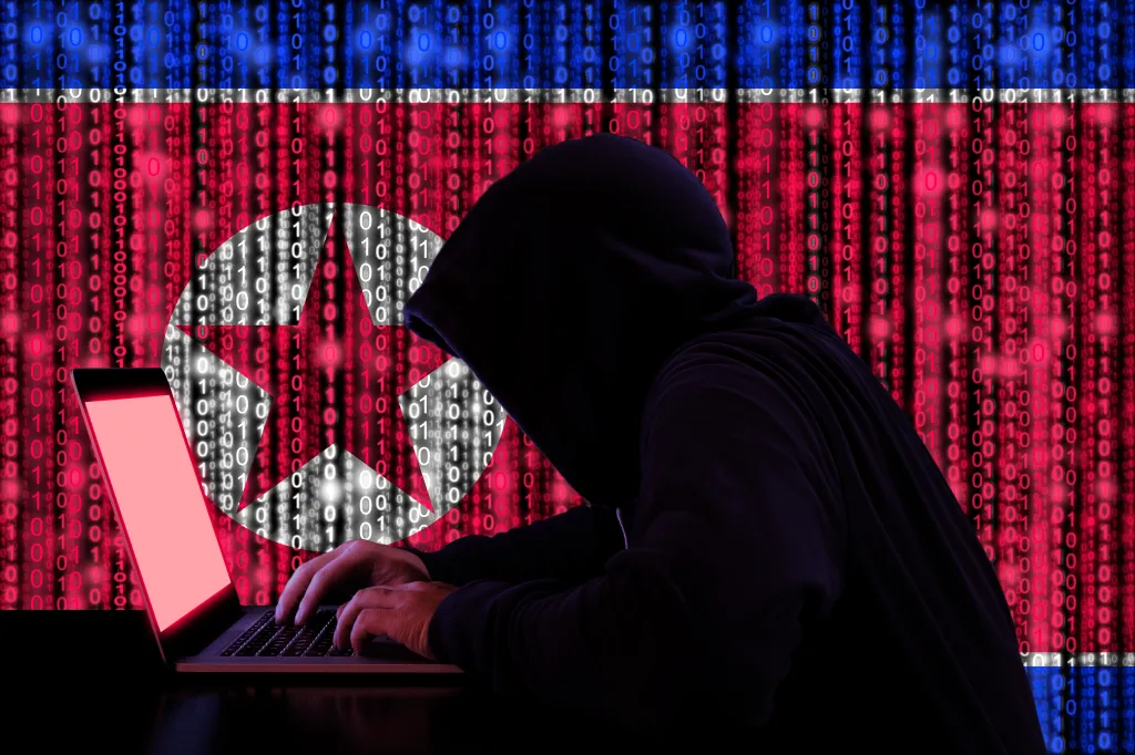 Illustration of a hooded figure typing on a laptop with a digital North Korean flag in the background.
