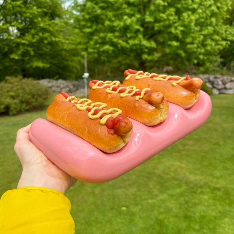 A pink serving platter with three hot dogs on it. 
