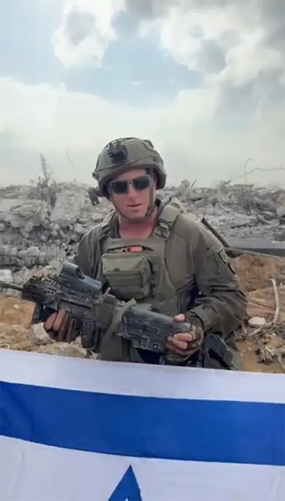 An IDF soldier holding a Tavor rifle in front of rubble, with an Israeli flag at the bottom of the frame.