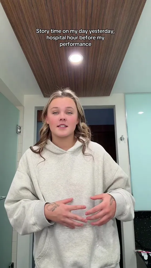 JoJo Siwa in a light gray hoodie talking about being rushed to the hospital.