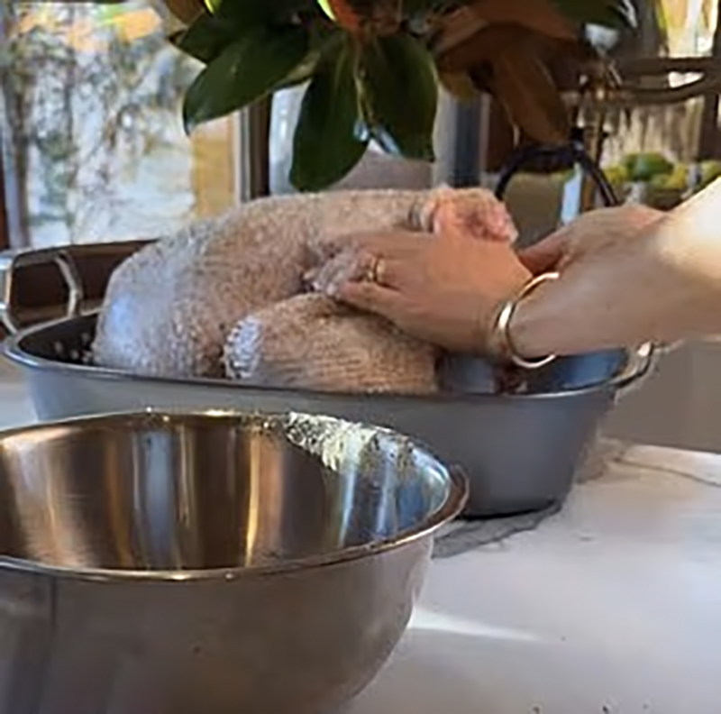 Meghan Markle preparing a raw turkey, wearing a gold bracelet and ring without gloves.