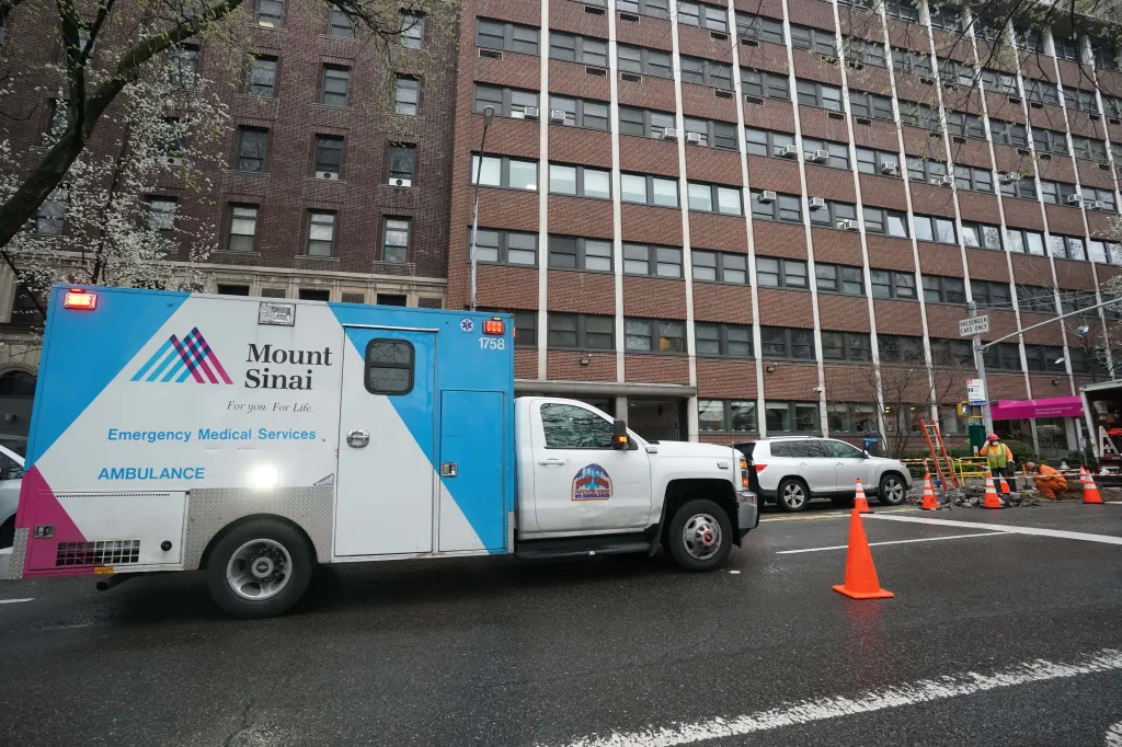 A Mount Sinai Emergency Medical Services ambulance on a city street next to a brick building.