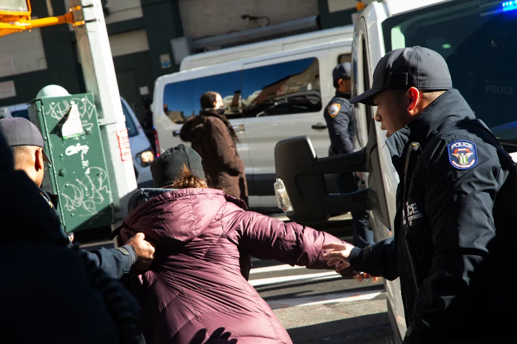 Two NYPD officers attempting to clear a protester in a maroon jacket from the street.