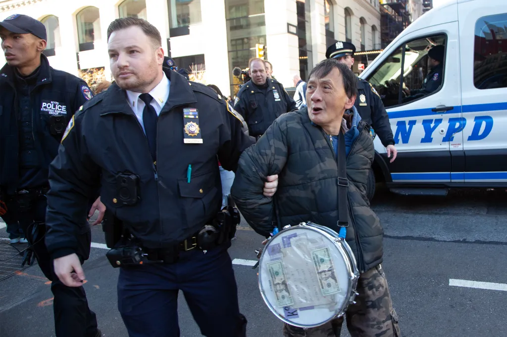 NYPD officers arresting a man with a drum attached to his body.