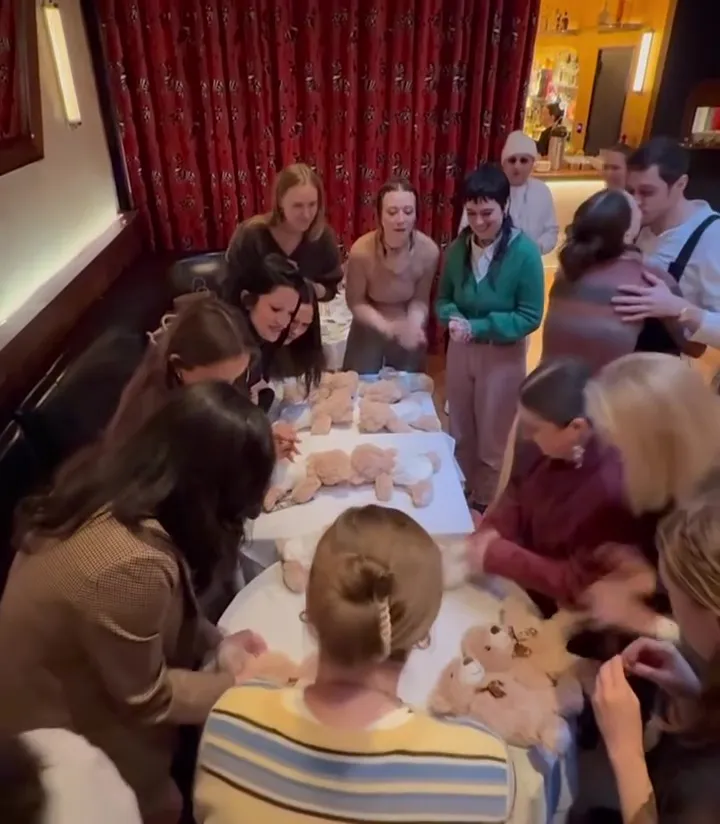 People surrounding tables covered with teddy bears and diapers, with Pete Davidson kissing Elsie Hewitt in the background.