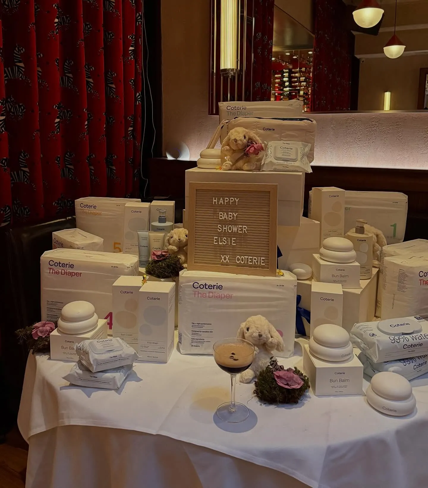 Baby shower display with Coterie diapers, creams, and wipes, and a sign that reads