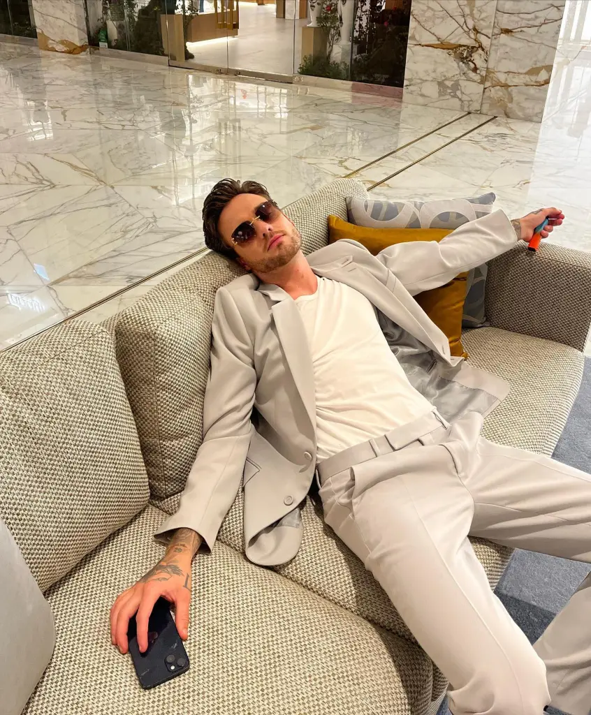 Liam Payne lounging on a couch in a light gray suit, white t-shirt, and sunglasses.