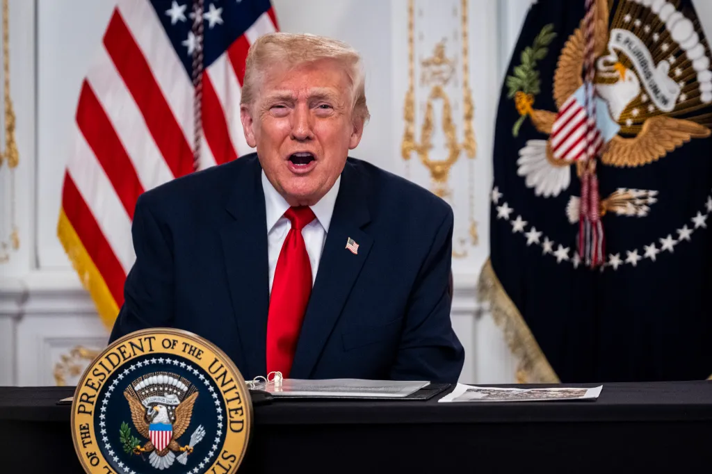 President Donald Trump speaking from a table with the presidential seal.