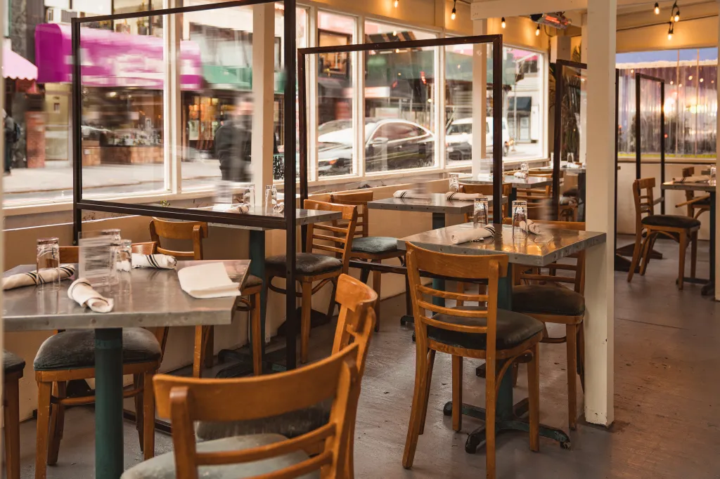 Outdoor dining area of a New York City restaurant set up on a sidewalk with empty tables and transparent partitions.
