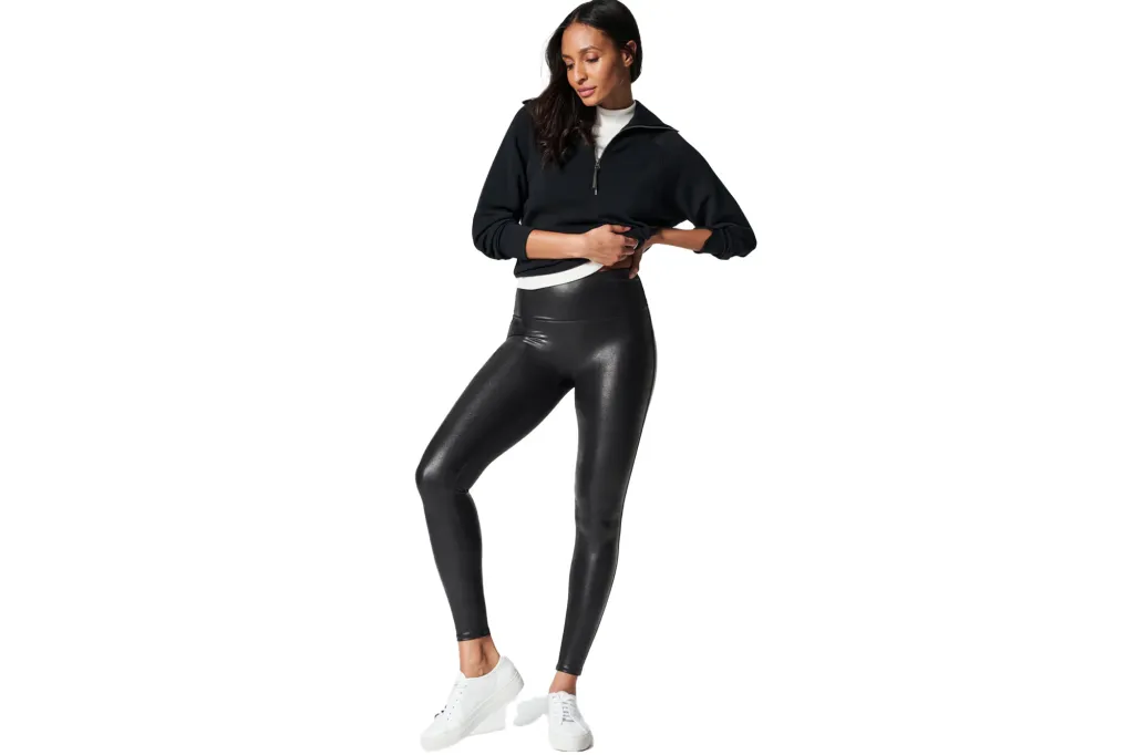 Woman wearing a black half-zip sweatshirt, white top, and black faux-leather leggings with white sneakers.