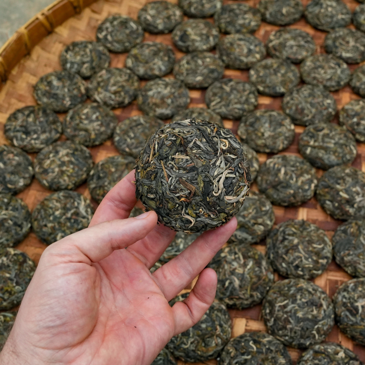 A hand holding loose-leaf tea above a basket of loose-leaf tea.
