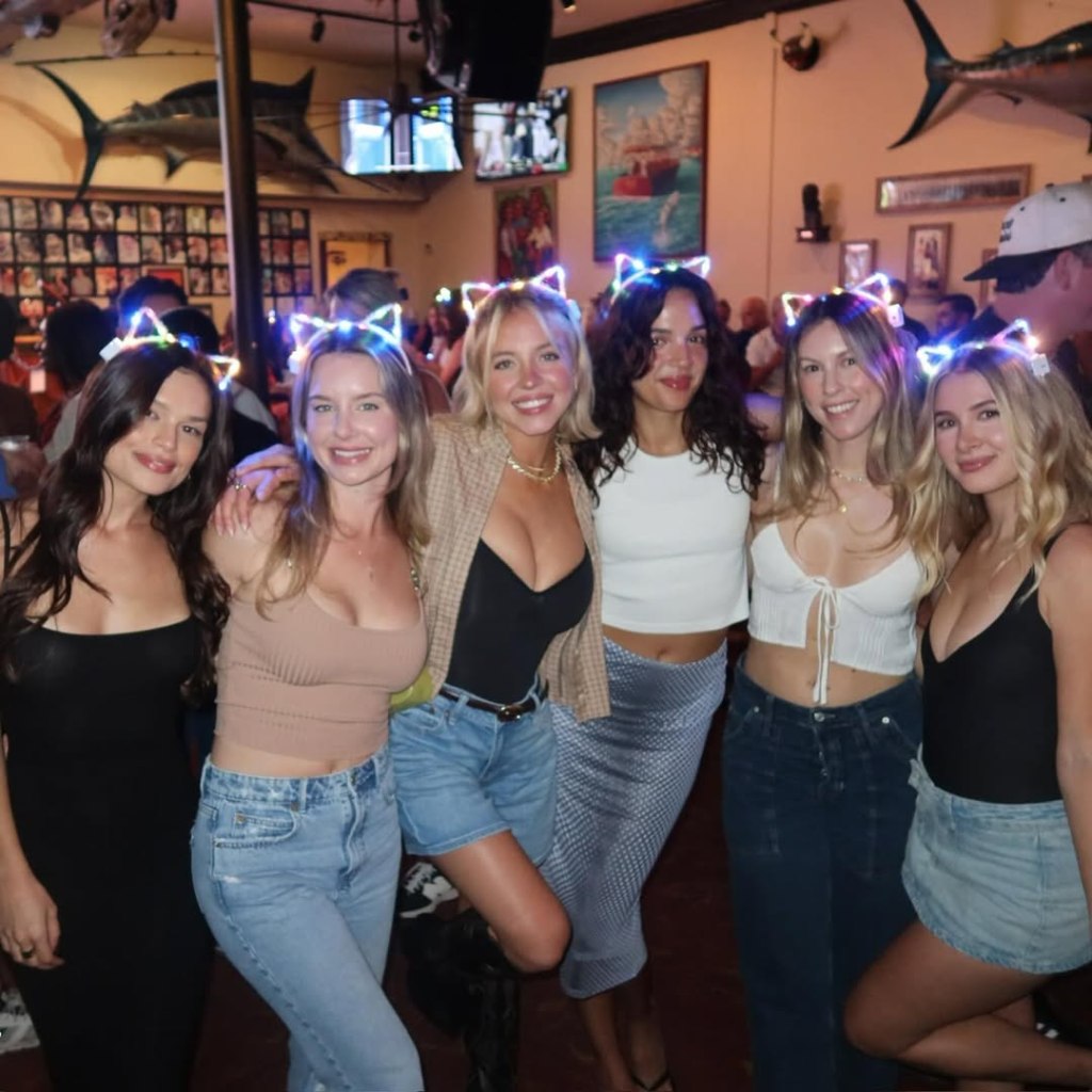 Six women, including Sydney Sweeney, posing for a photo while wearing light-up cat ears.
