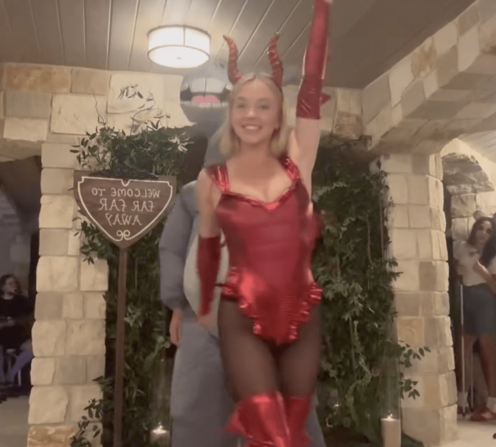 Sydney Sweeney dressed as a sexy dragon in a red bodysuit with horns and arm-length gloves.