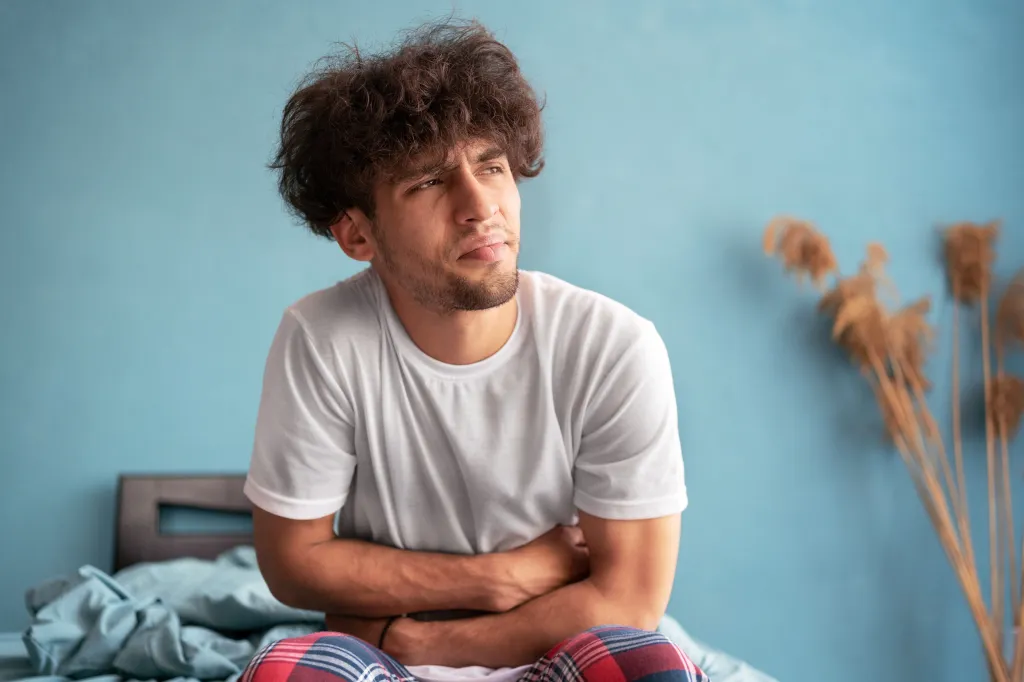 Young Arab man suffering for stomach ache sitting on bed at bedroom. 