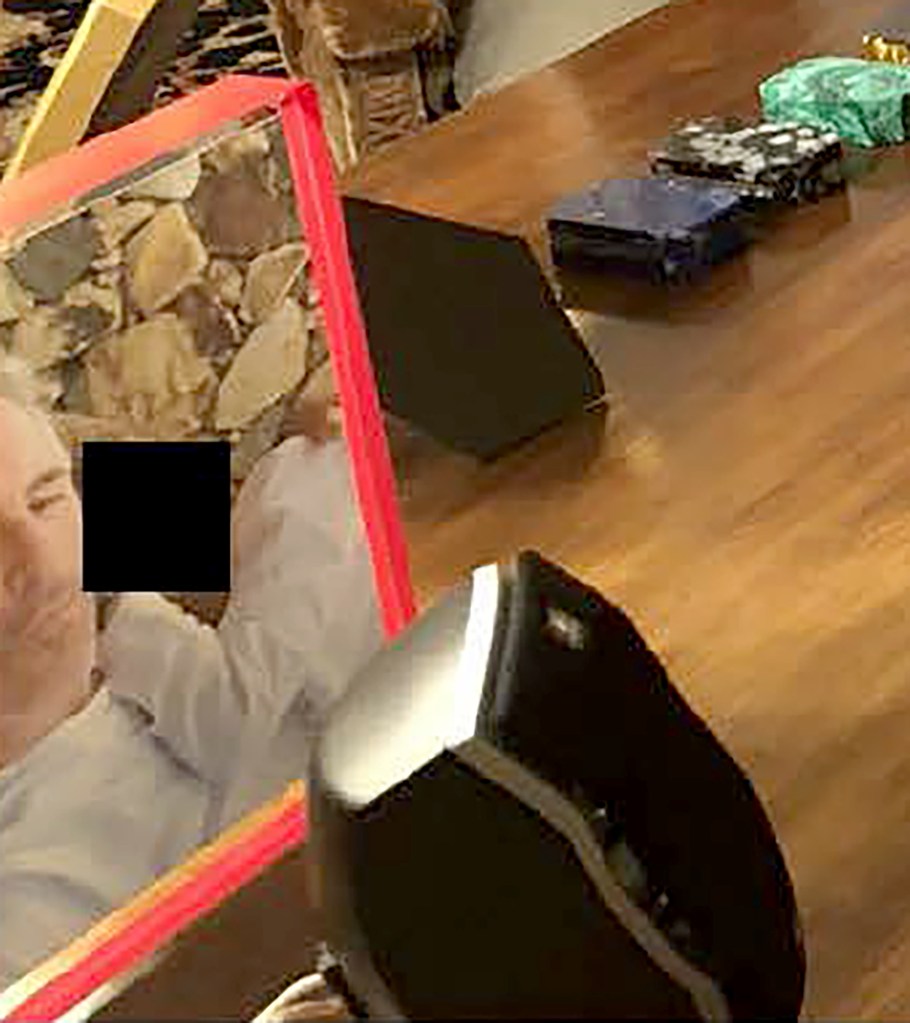 Blurred image of a man, possibly Jeffrey Epstein, at a table with various objects including what appears to be socks and a computer mouse.