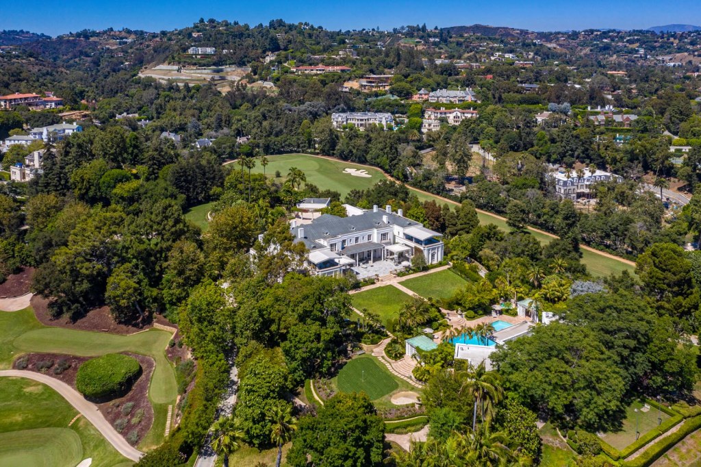 Aerial view of the 1930s Bel-Air estate on Bellagio Road with a large white mansion, extensive green lawns, swimming pools, and a golf course, surrounded by trees and other homes in the hills.