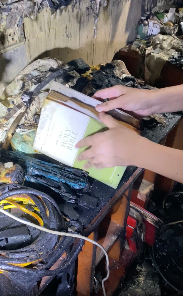 Hands retrieving an intact Bible from fire debris.