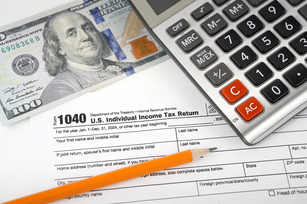 A 2024 U.S. individual 1040 tax form, a calculator, a $100 bill, and a pencil.