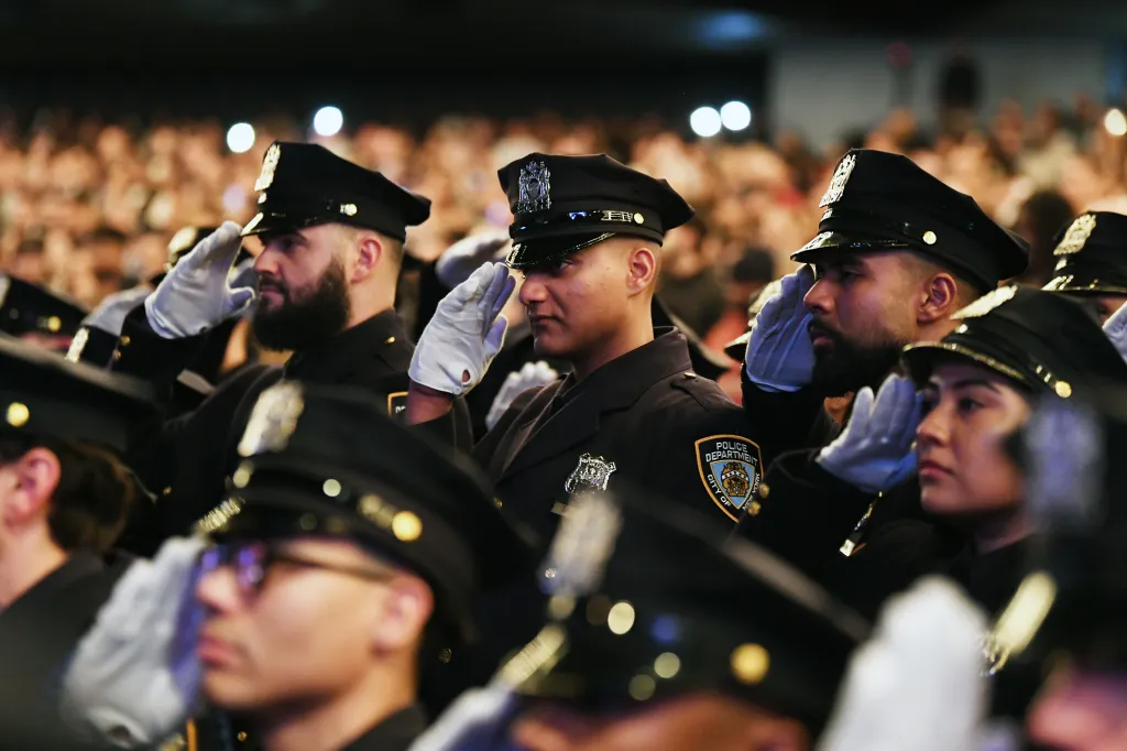 NYPD graduates in uniform saluting at a ceremony.