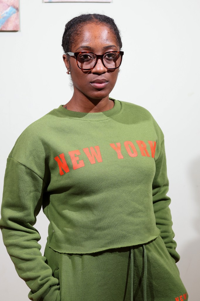 Elizabeth Fleurisma, wearing a green New York sweatshirt and glasses, poses for a photo.